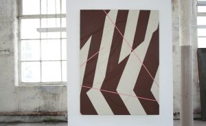 An image of a painting in a gallery. The painting features brown and cream geometric lines.