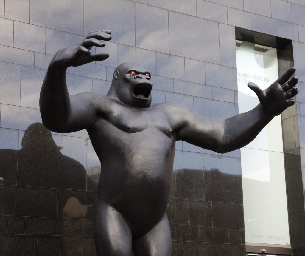 A sculpture of the gorilla character King Kong. The gorilla's arms are outstretched. The background is a black tiled building.