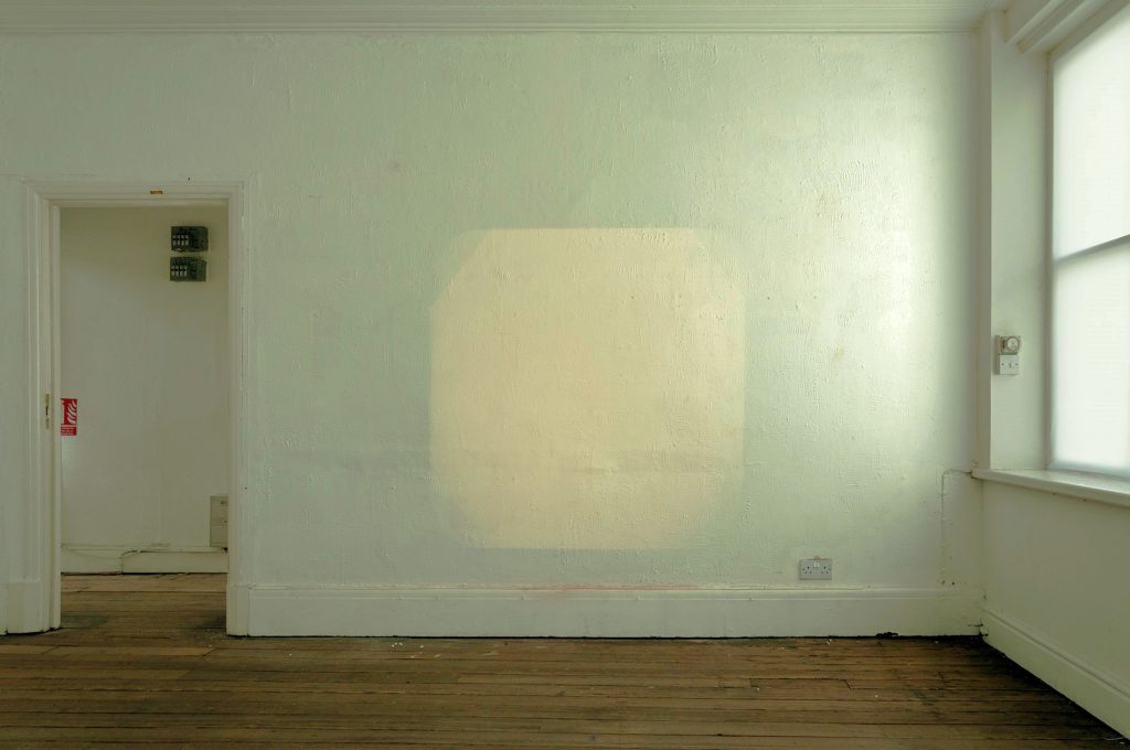 A pale green wall, with a roughly square patch of pale yellow.