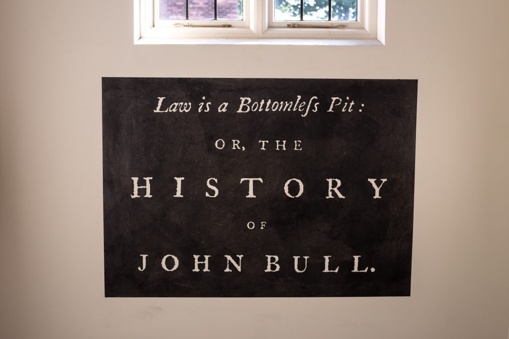 A vinyl applied to a wall that reproduces the title of a book: 'Lsaw is a bottomless pit: or, the History of John Bull.'