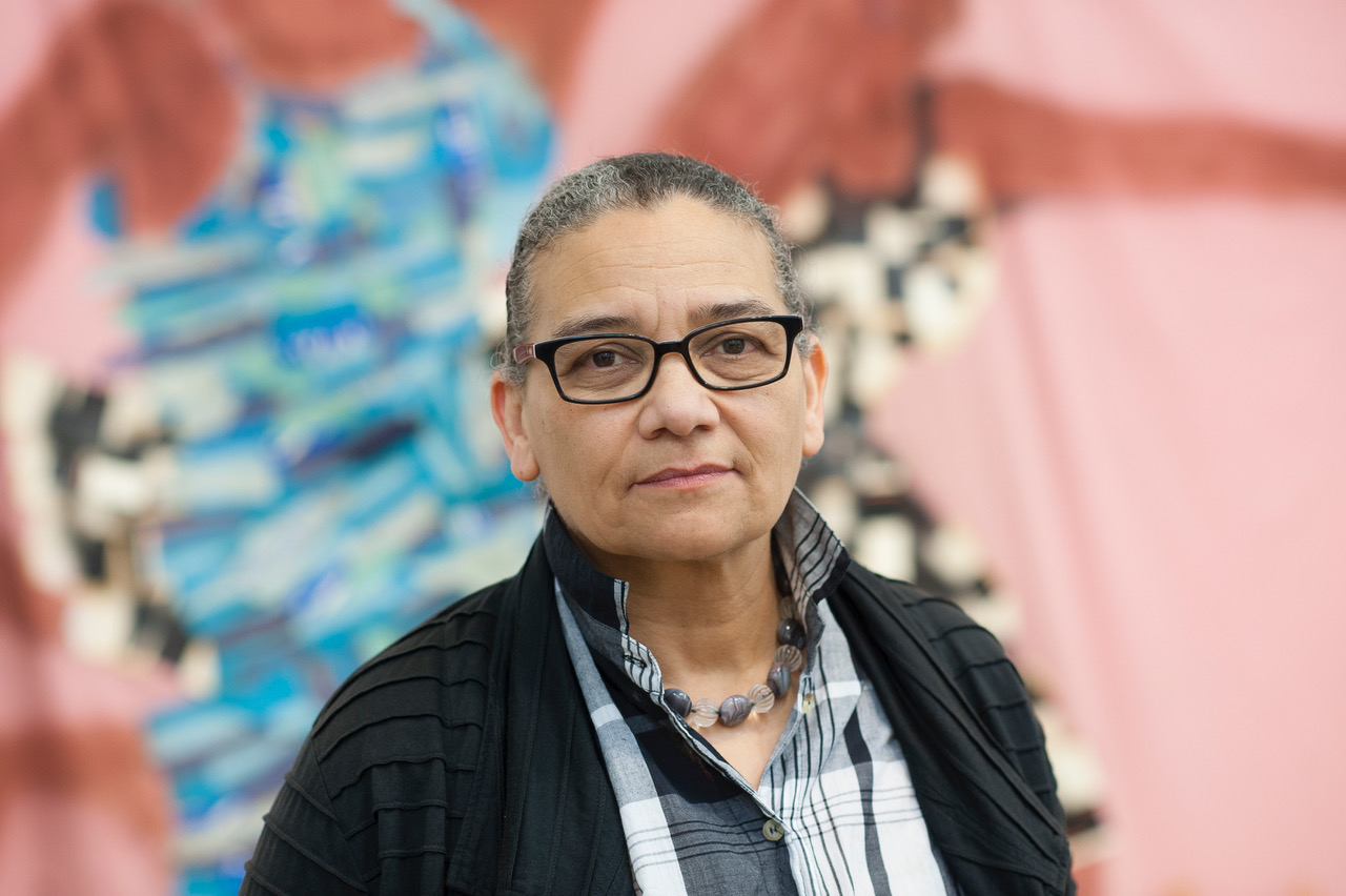 Photographic portrait of the artist Lubaina Himid, a black woman wearing glasses, a grey checked shirt and a dark jacket.