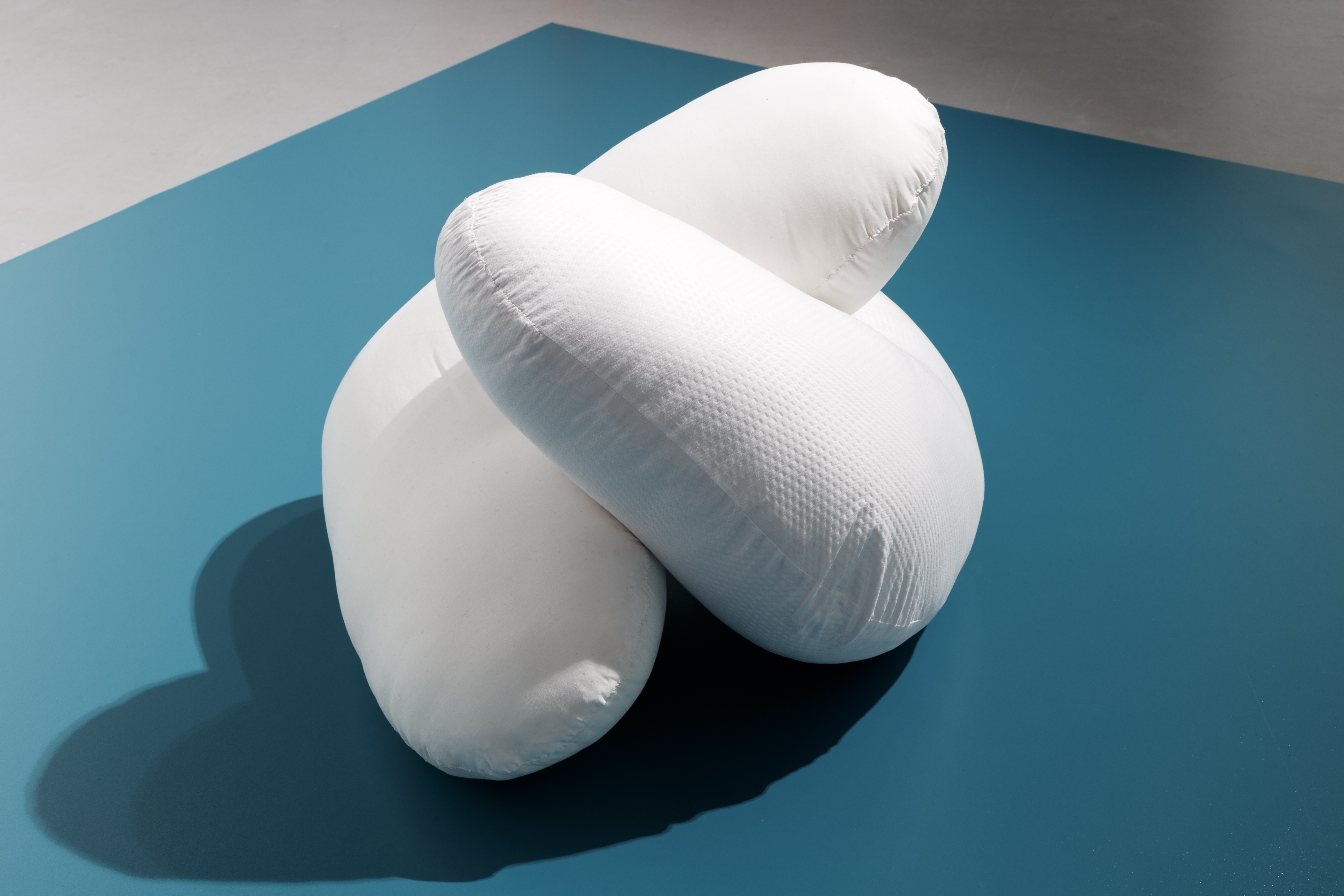 Two soft white shapes interlocking, as though embracing. They rest on a blue plinth.