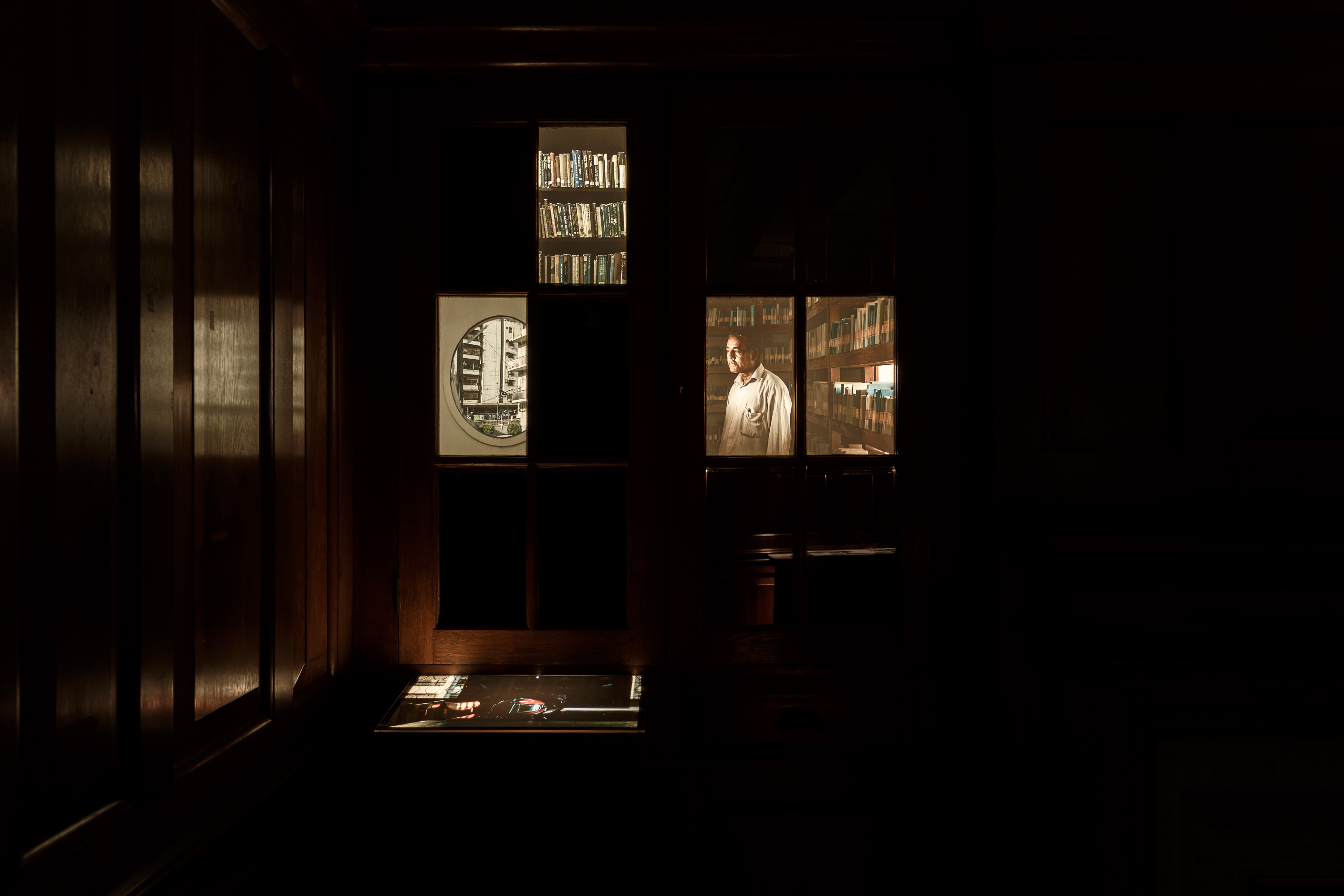 A darkened room with three artist's films showing a man, some bookshelves and a view through a round window.