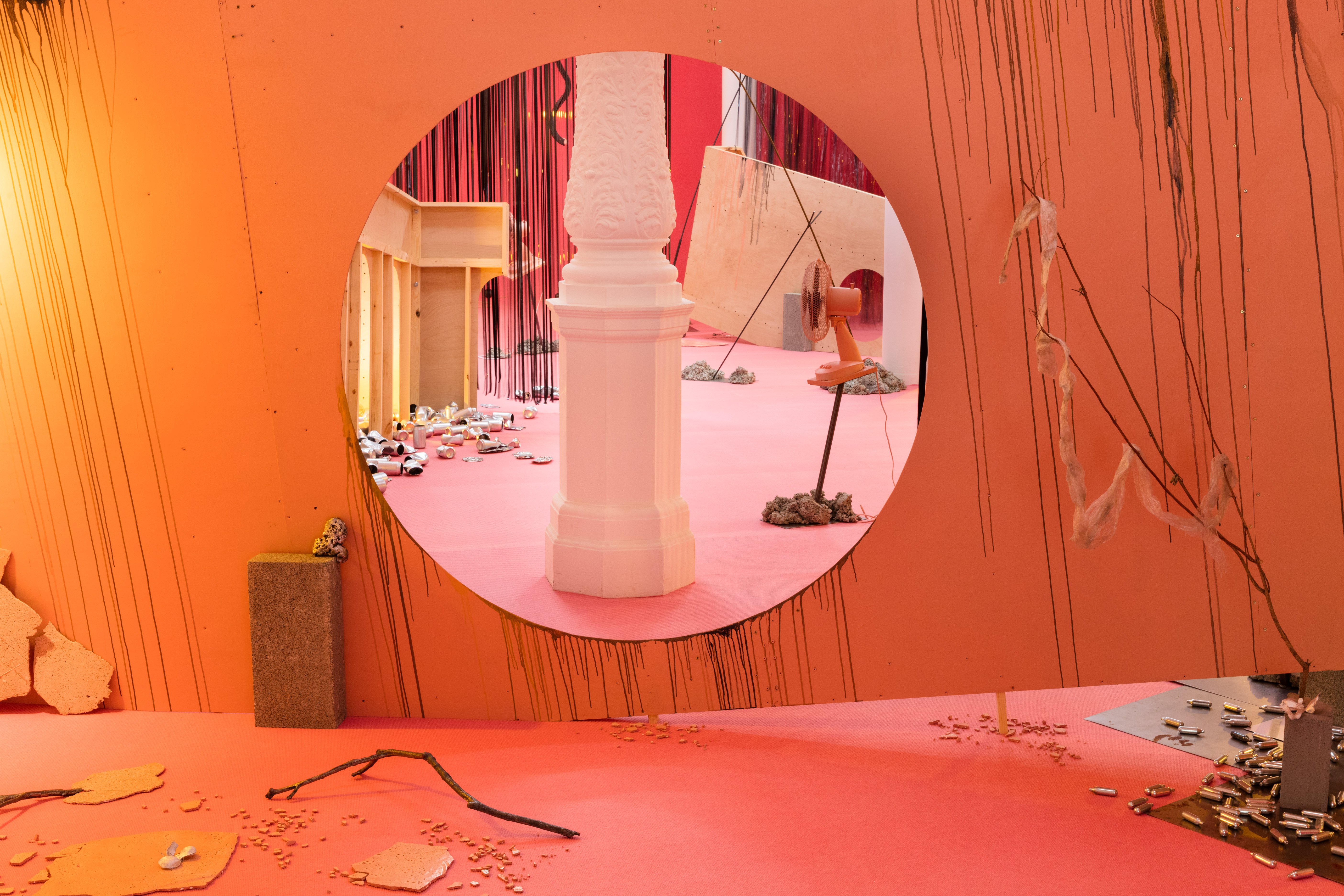 A room suffused with orange and peach light. In a circle, a view of a pillar is visible. Several objects such as a twig are visible resting on the floor.