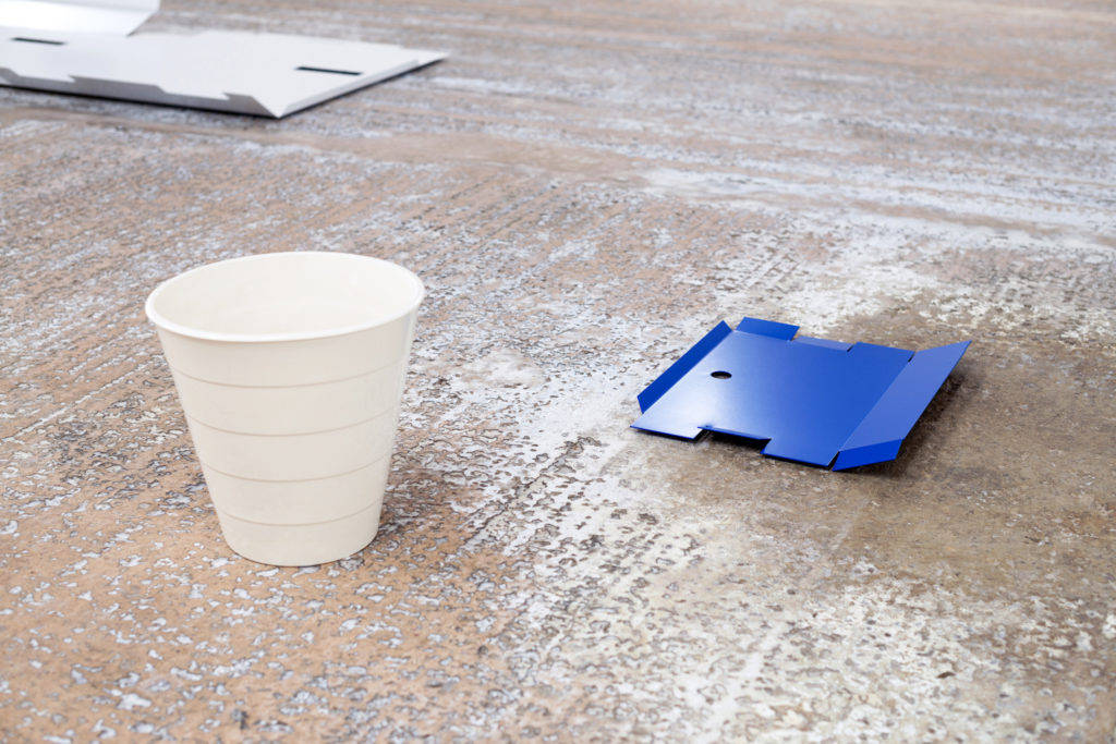 A stone floor with a white wastepaper bin and a piece of blue cardboard.