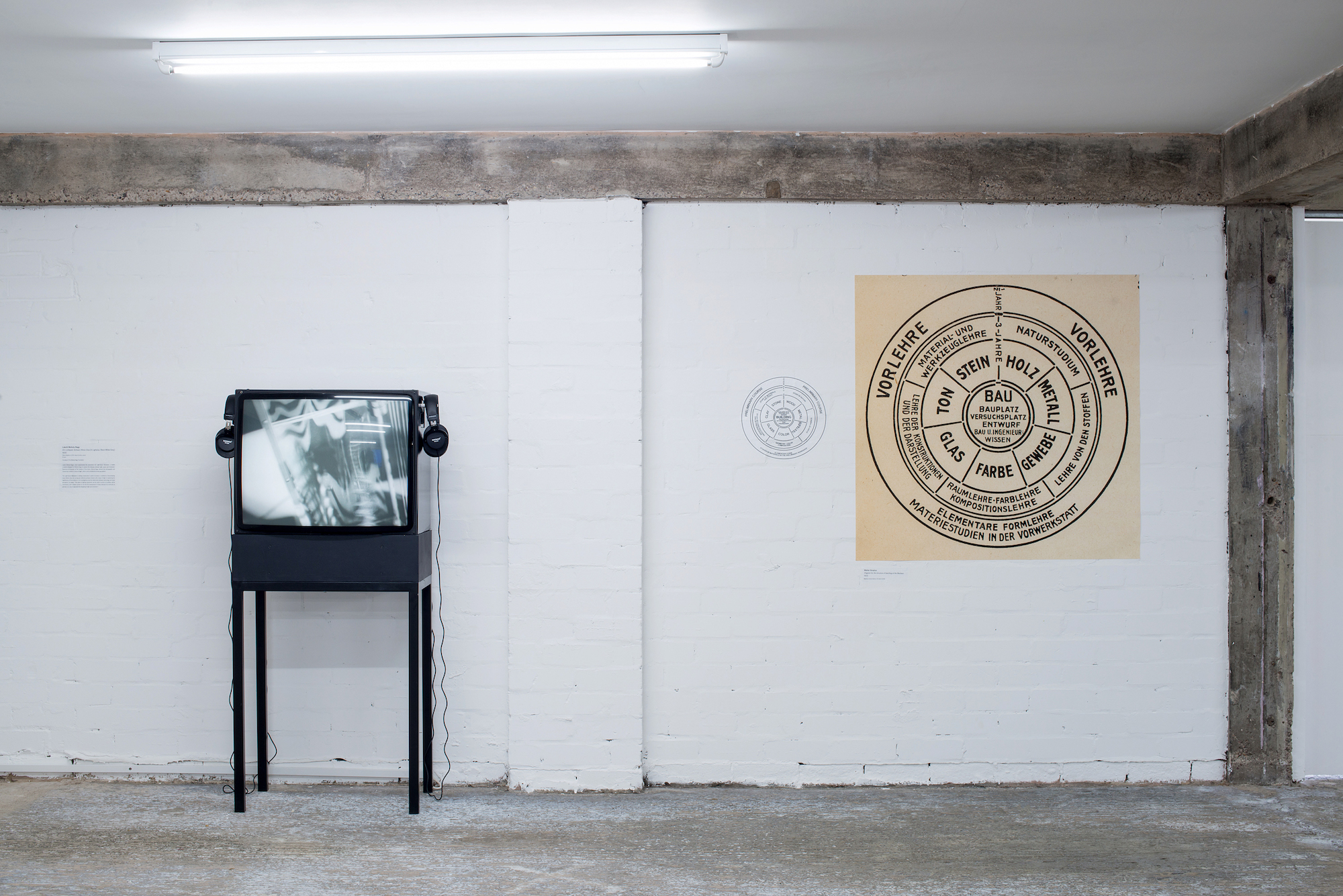 Two artworks in a gallery. On the left, a TV screen with headphones shows an artist's film. On the right, a spiral diagram in German.