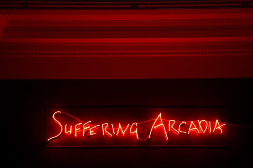 Neon red writing that reads: 'Suffering Arcadia'.
