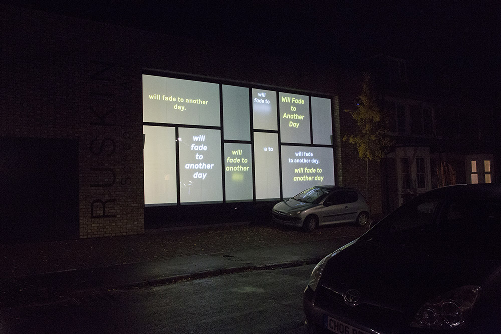 An image of windows, lit from the inside, on a dark night. The windows feature short poetic texts, in white and yellow font.