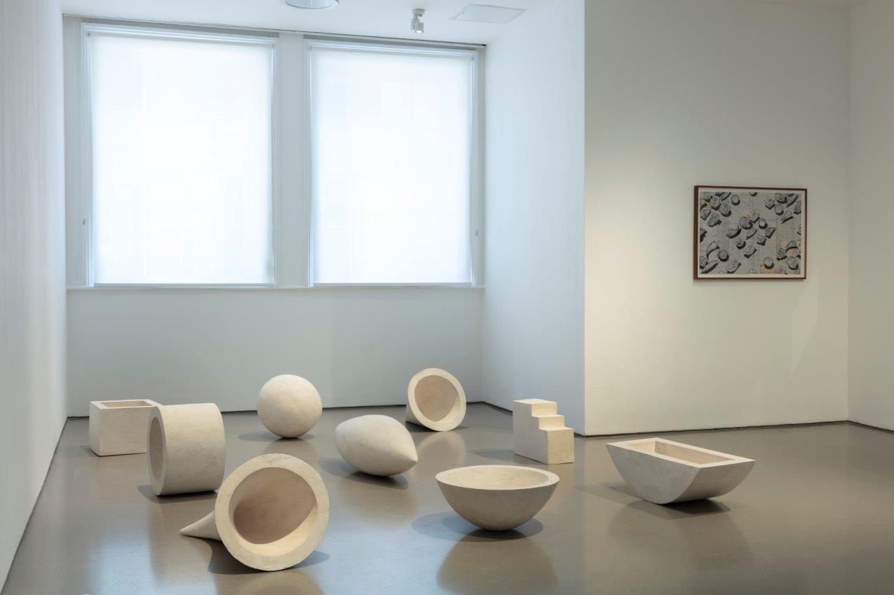 A series of white abstract and geometric sculptures in a white gallery space.