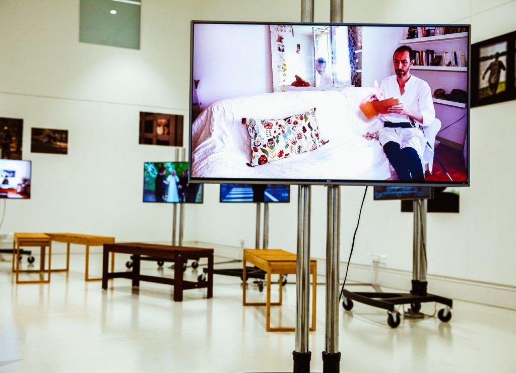 A gallery space with several TV screens showing artist films. Benches can be seen in the background.