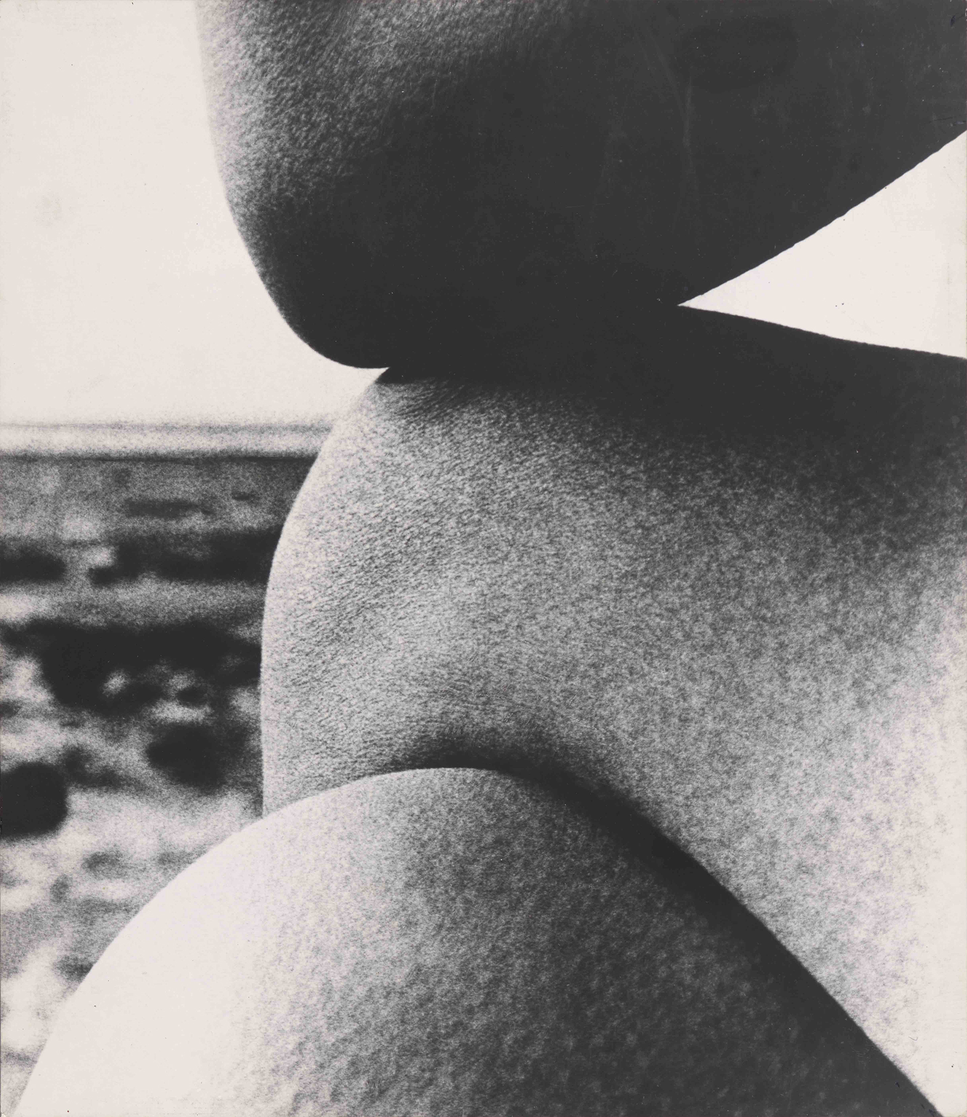 A black and white image showing crossed legs and an elbow. The image is zoomed in so the flesh might be rocks or pebbles.