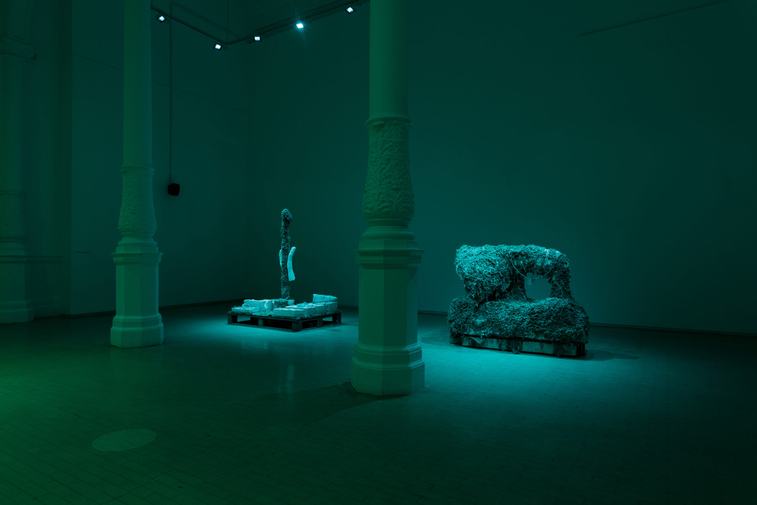Two sculptures resembling an underwater wreckage sits in the centre of a green-lit gallery space.