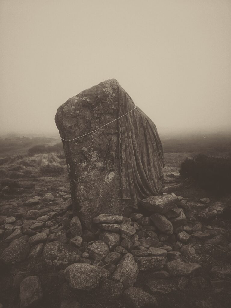 A sepia photograph of a standing stone with a lace cloak tied around it.