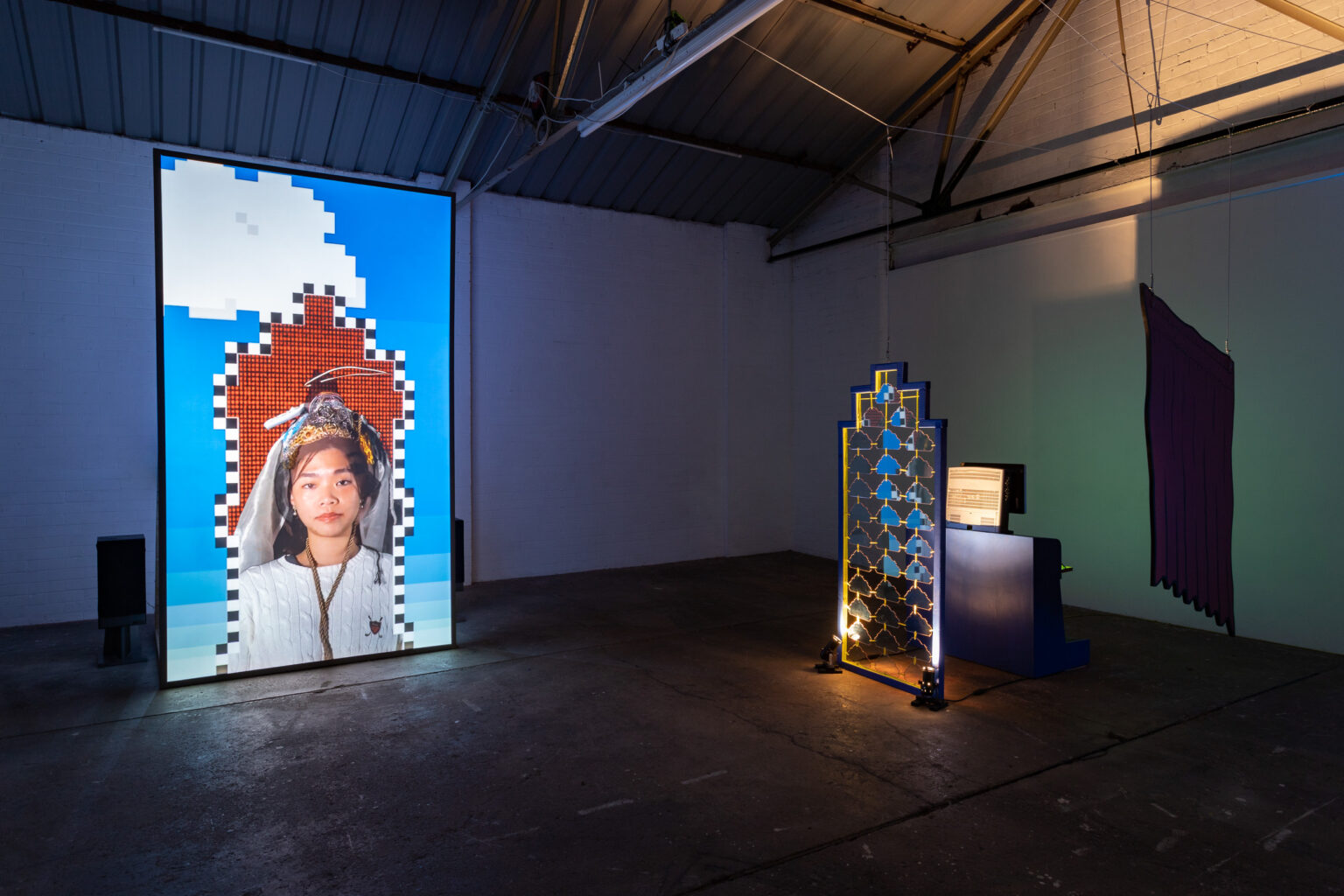 A vertical screen showing a figure in a medieval-inspired dress, framed in a pixelated arch. To the right is a doorframe filled with perspex clouds held together in a grille structure. Behind is a computer terminal and a hanging painted curtain.