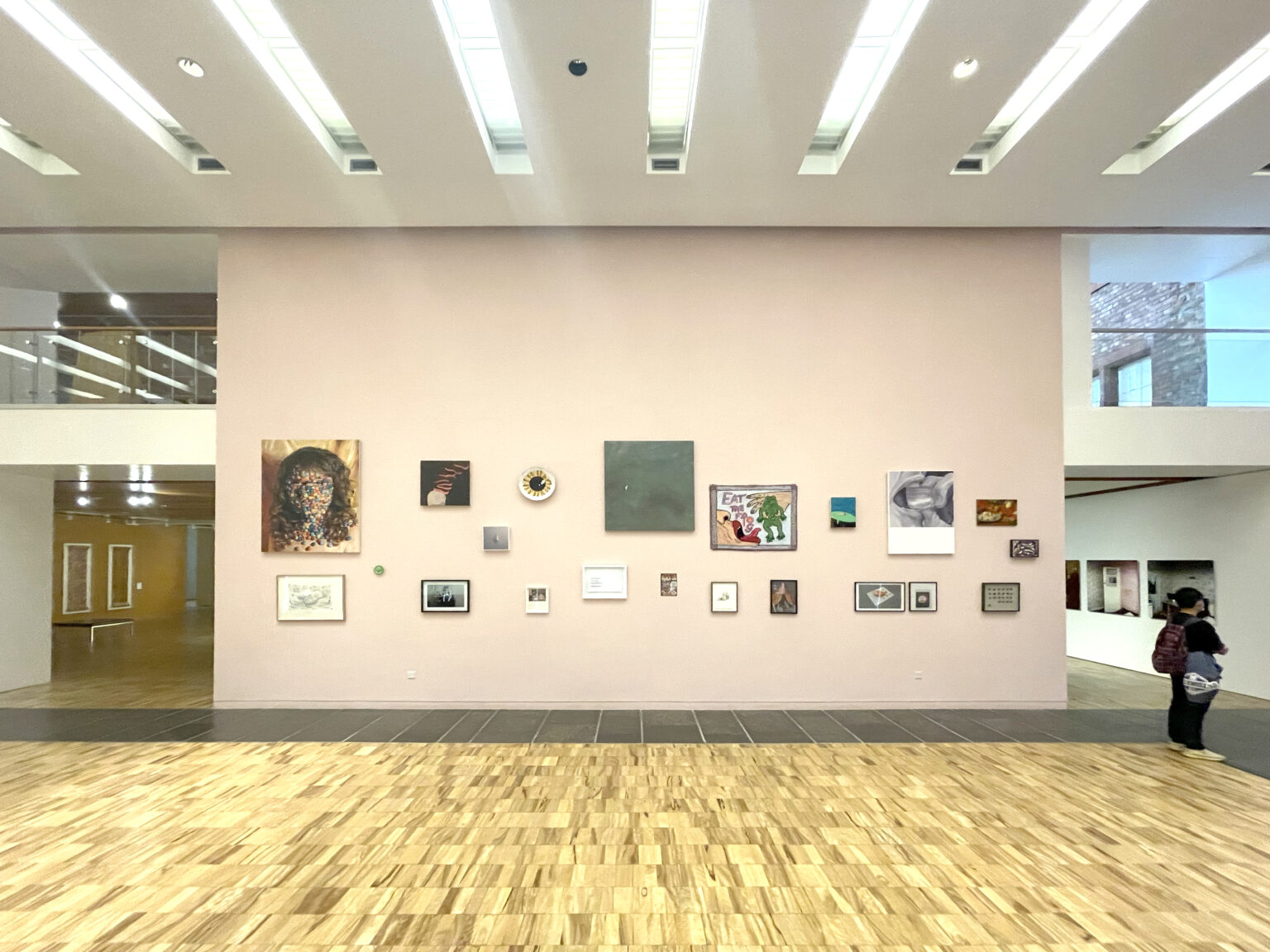 A series of works are shown in the centre of the image installed at different heights on a pastel pink wall.