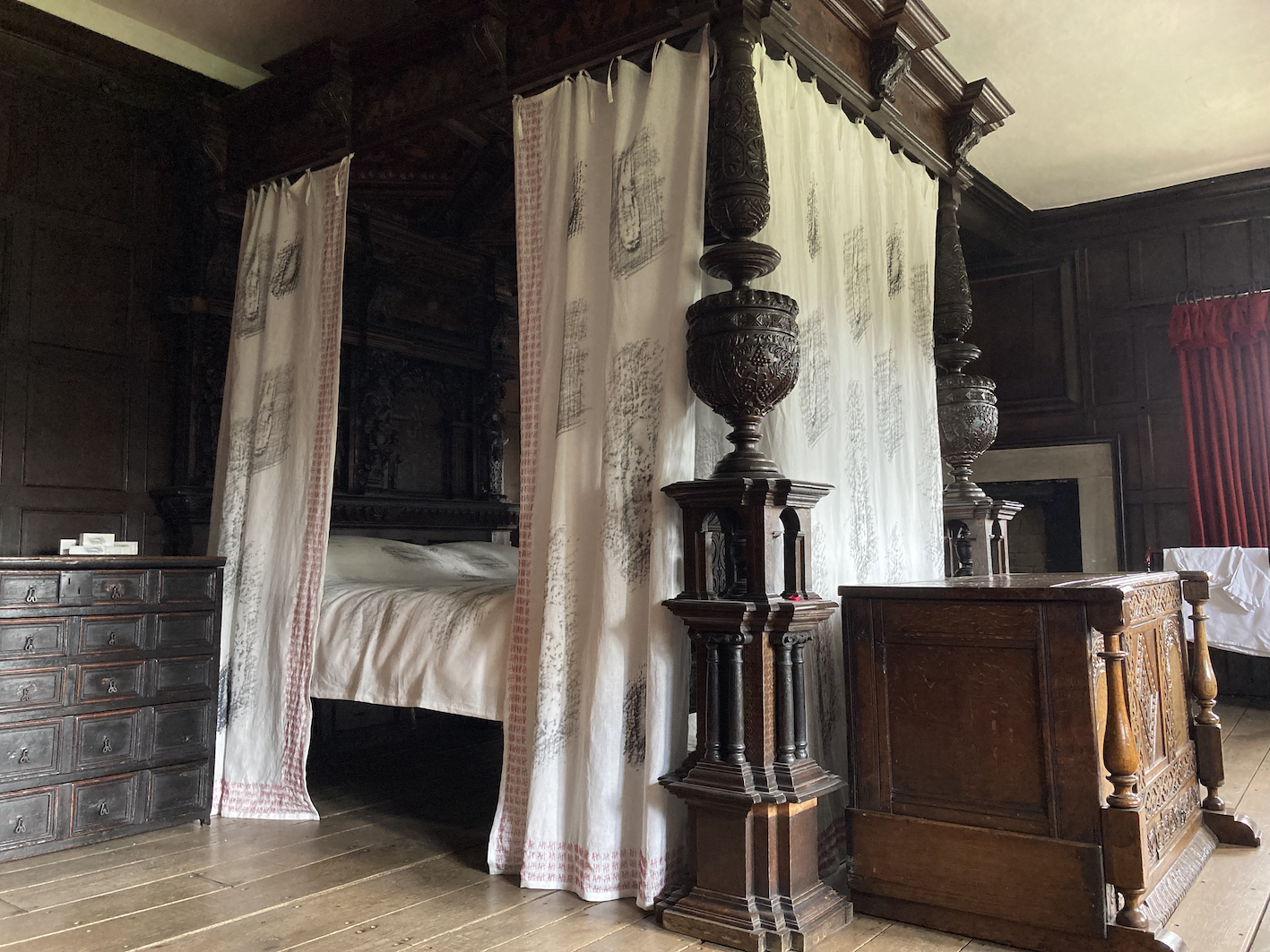 white drapes with a printed pattern hang around an old dark canopy bed in a historic room