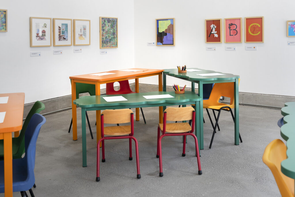 Photograph of the Artist Studio in the exhibition, showing tables, chairs, and artwork on the walls.