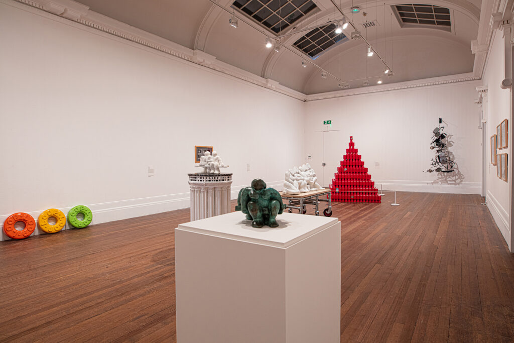 A photograph of the exhibition with a small jade-coloured figurine on a white plinth in the foreground