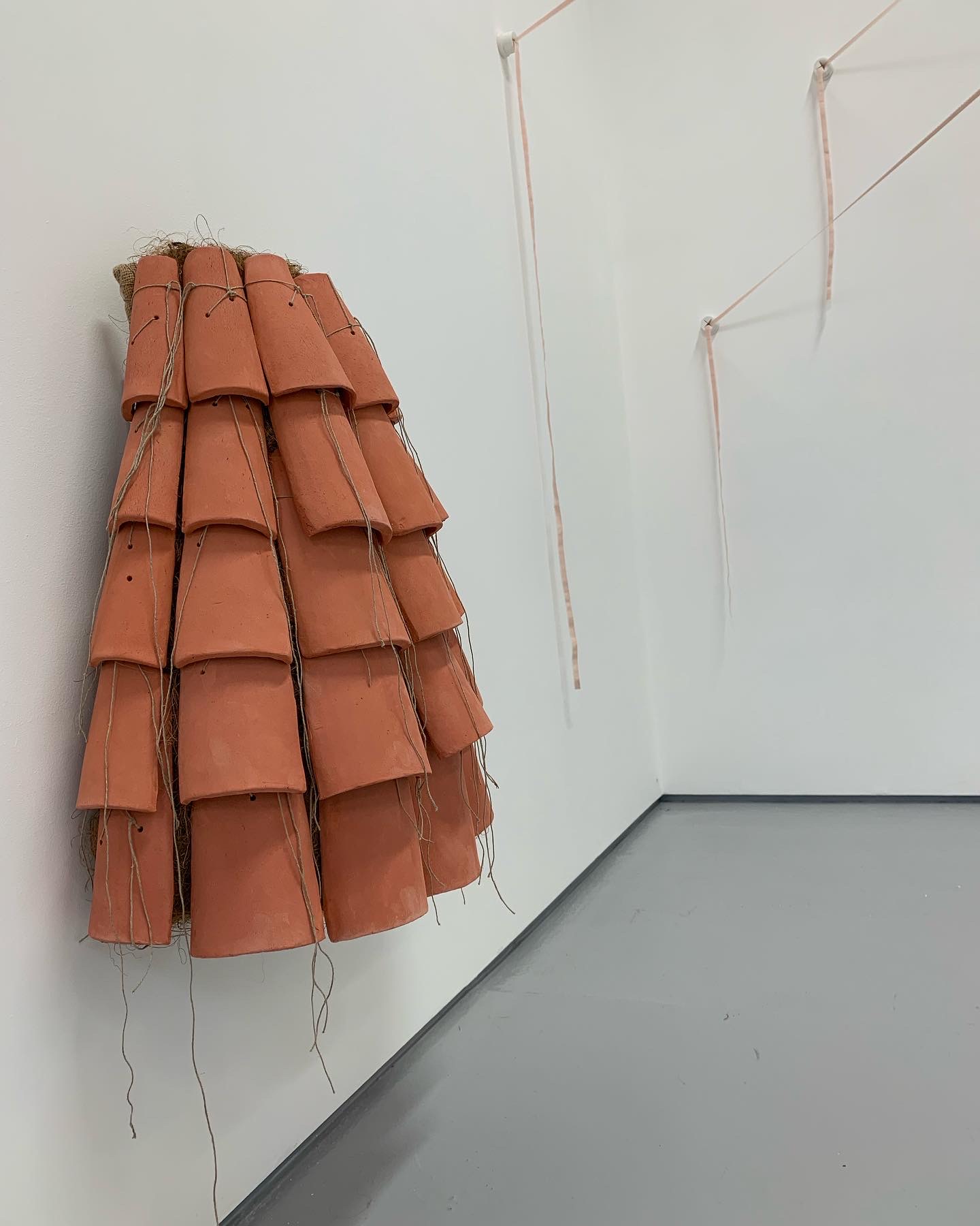 A wall hung sculpture made of terracotta tiles in the shape of a skirt.