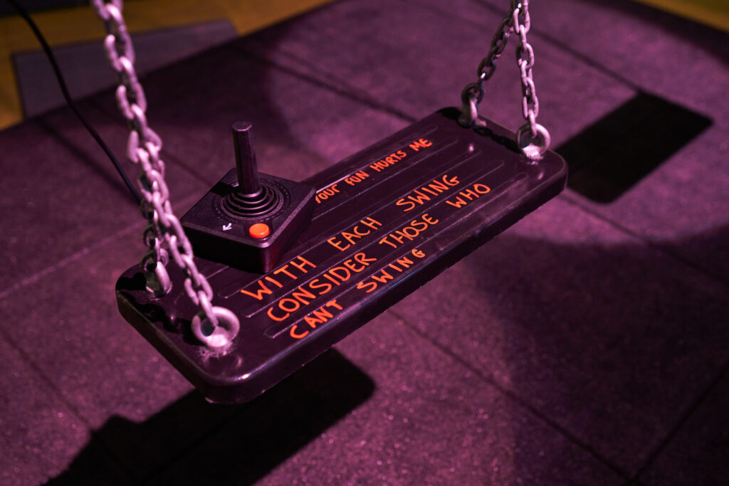 The seat of a swing with a joystick on it and text that reads 'your fun hurts me / with each swing consider those who can't swing'