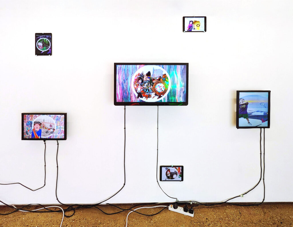 Six screens of varying size and orientation mounted on a white gallery wall. They each have a different image from 632700 on them; showing an abstract colourful background, a central white band with an image of a place inside, a photograph or hand drawn portrait on the left of the band and a photographed or hand drawn object on the right of the band. Cables hang down from some of the screens and snake across the floor.