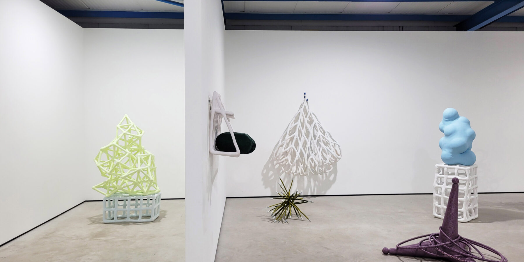 Sculptures in a white wall gallery space with a concrete floor and blue ceiling beams