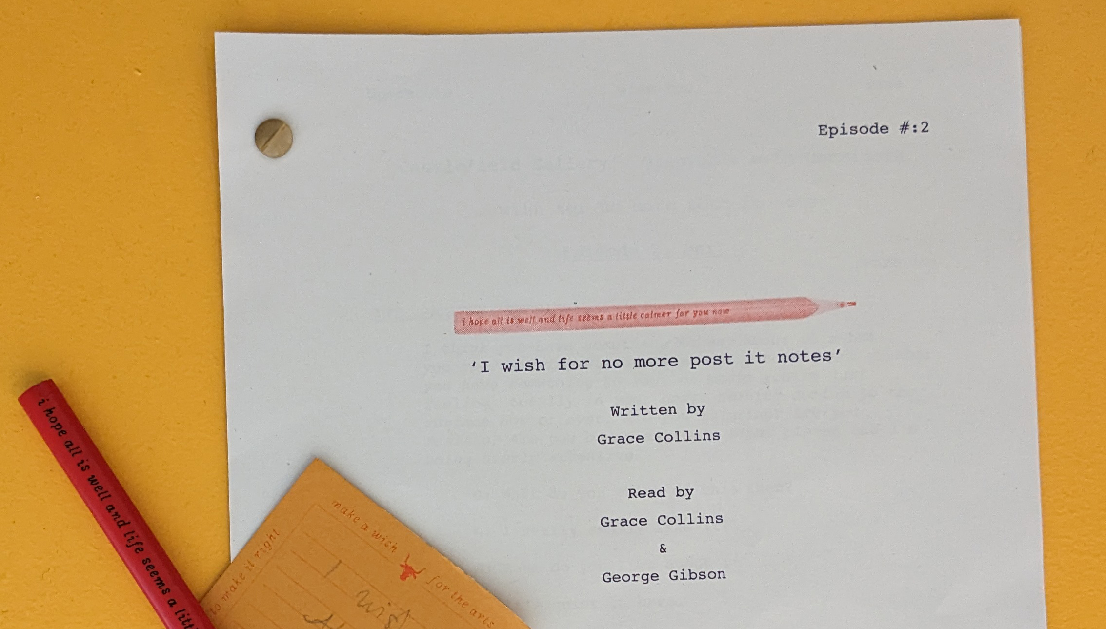A white typed page on a deep yellow background; the edge of an orange notebook and red strip of paper visible at the bottom left.