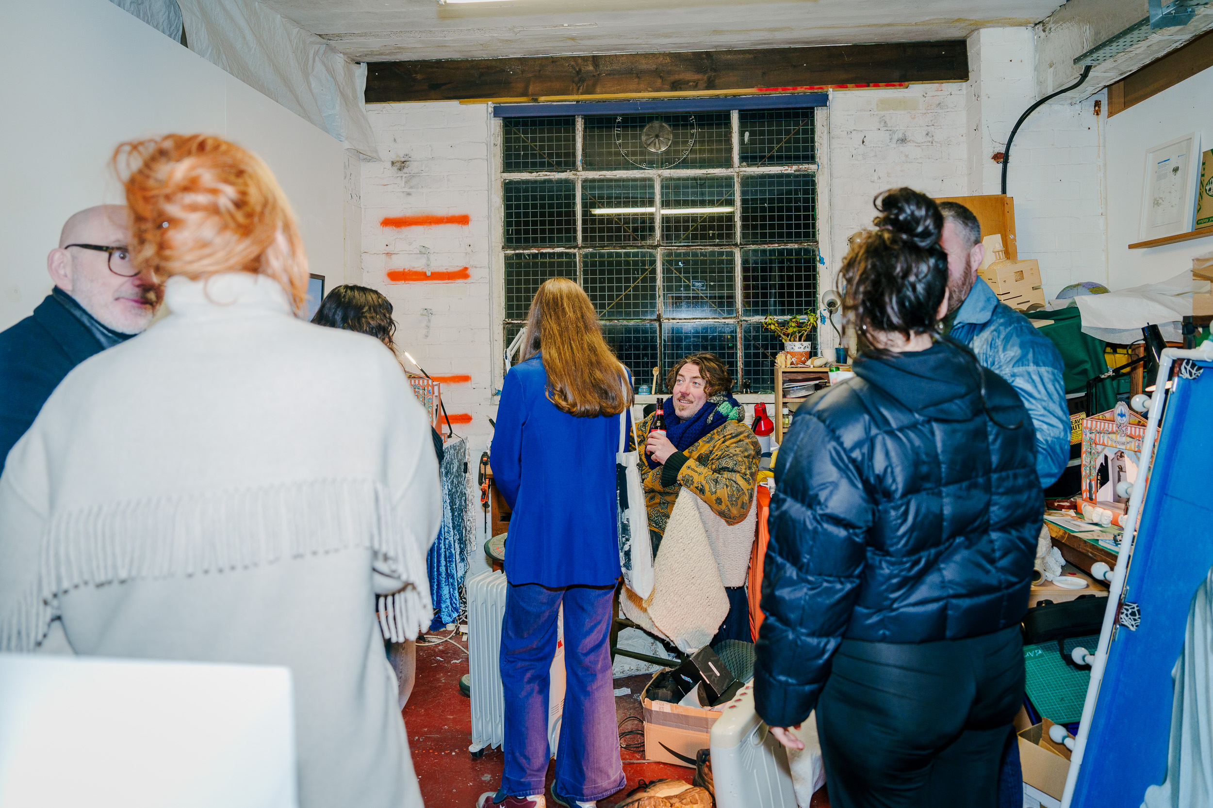 A group of people milling about and chatting in an artists studio.