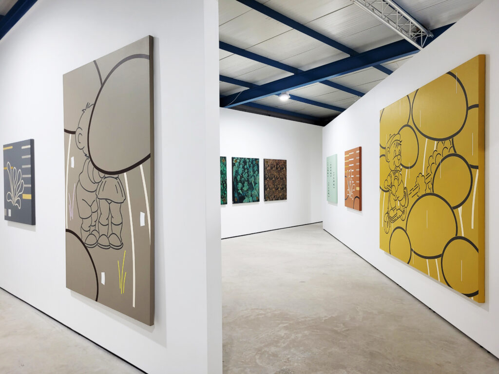 Two walls within the gallery space that have large paintings, grey on the left orange on the right, with bubble shapes on them