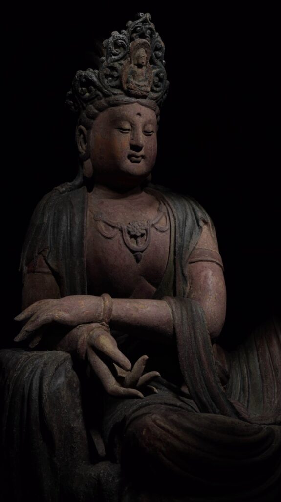 A film still in which the Bodhisattva is barely lit so the details are just visible against the black background