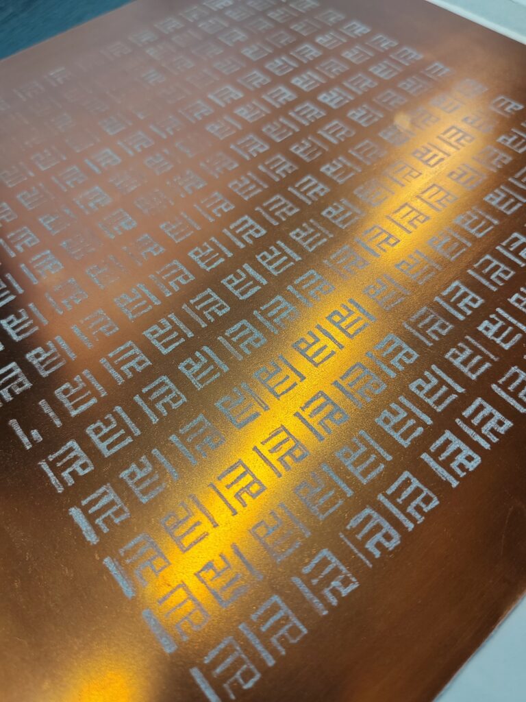 A sheet of shiny gold material with the underlined word 'me' repeated across it