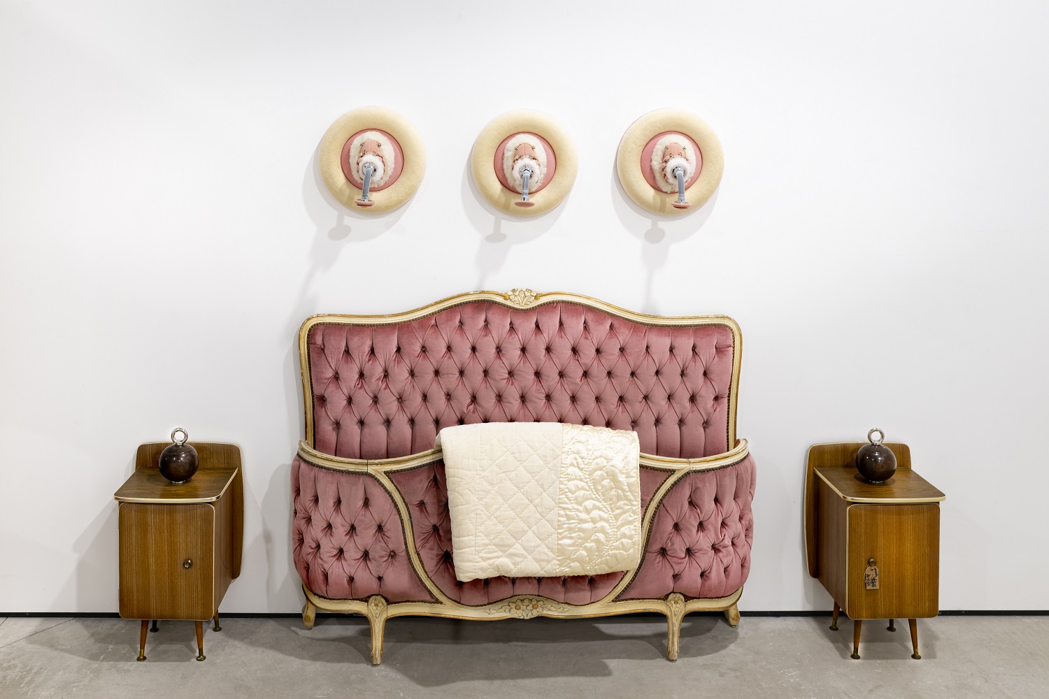 A bedroom scene where the plush velvet bed has been squished so its footboard touches its headboard and the spotlights above are kinky furry toys