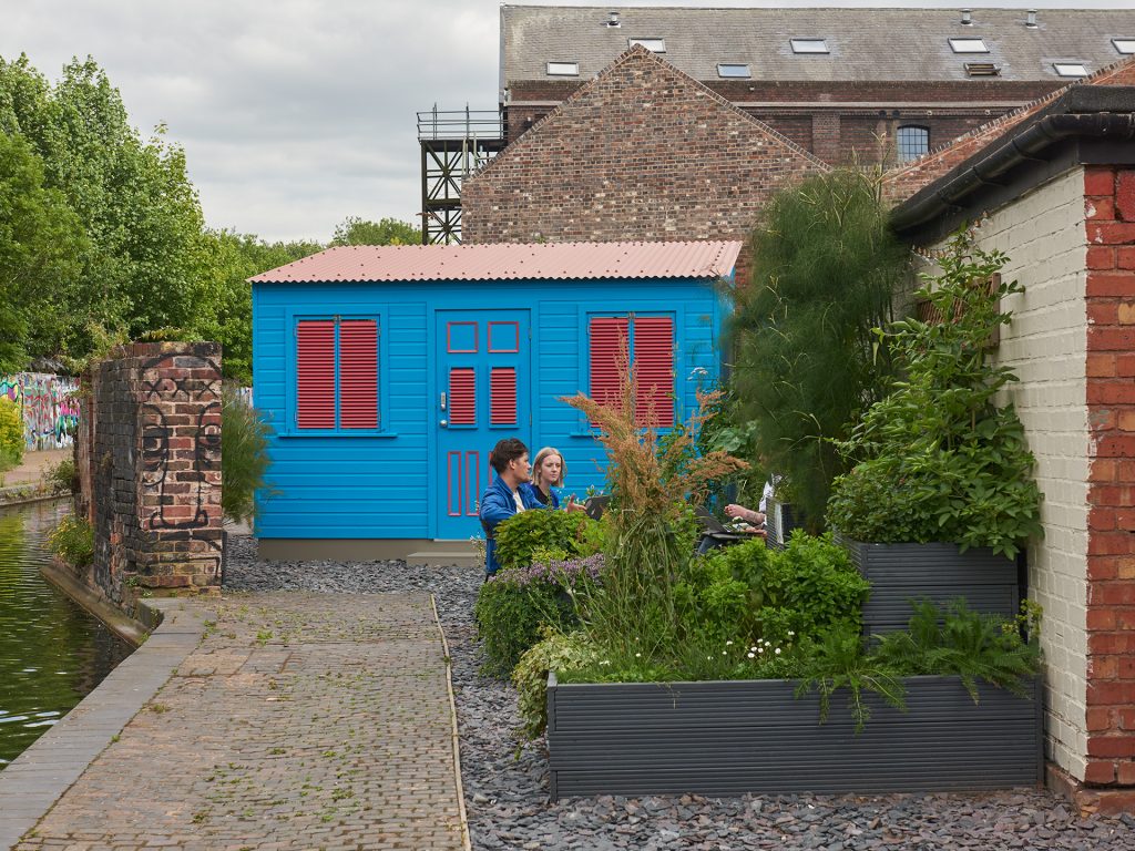 A bright blue and red shed besides the canal - an artwork by Alberta Whittle