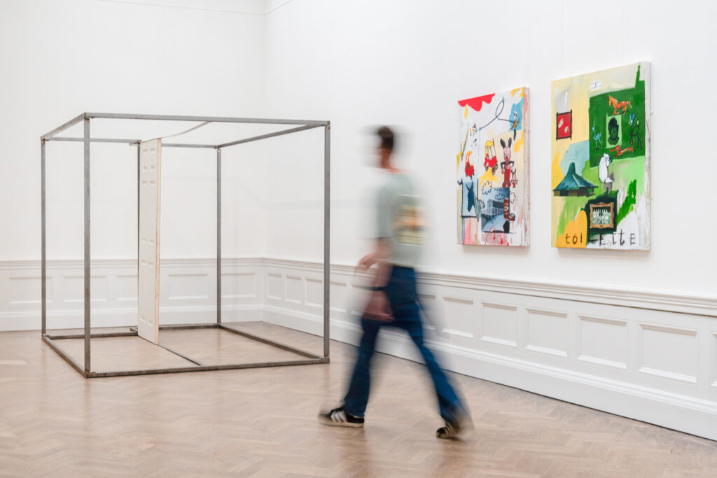 Installation shot. A man walk through the gallery space, to his right are two paintings.