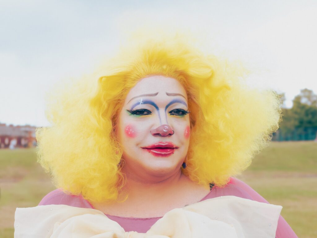 A clown with a curly blond wig, made-up face and pink dress