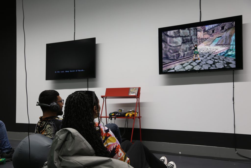 Two dark skinned people watch afilm installation. They are both sat on bean bags.