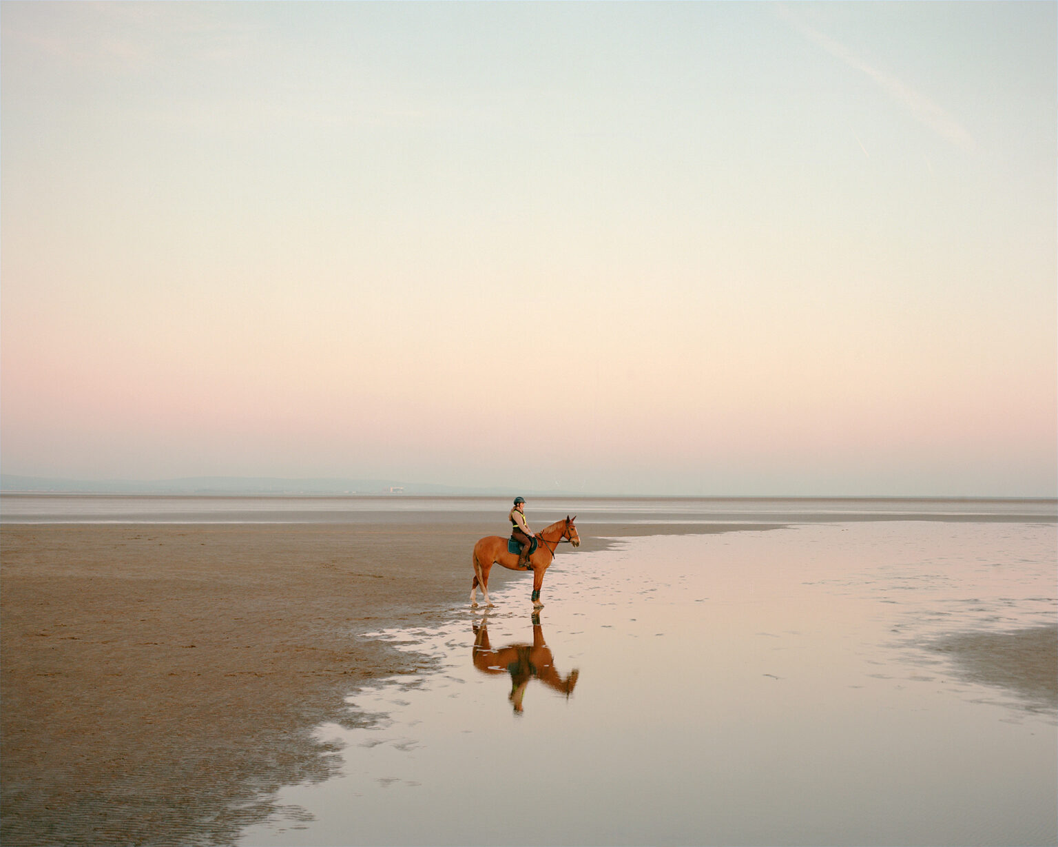 a horse rider standing still on calm wet sands