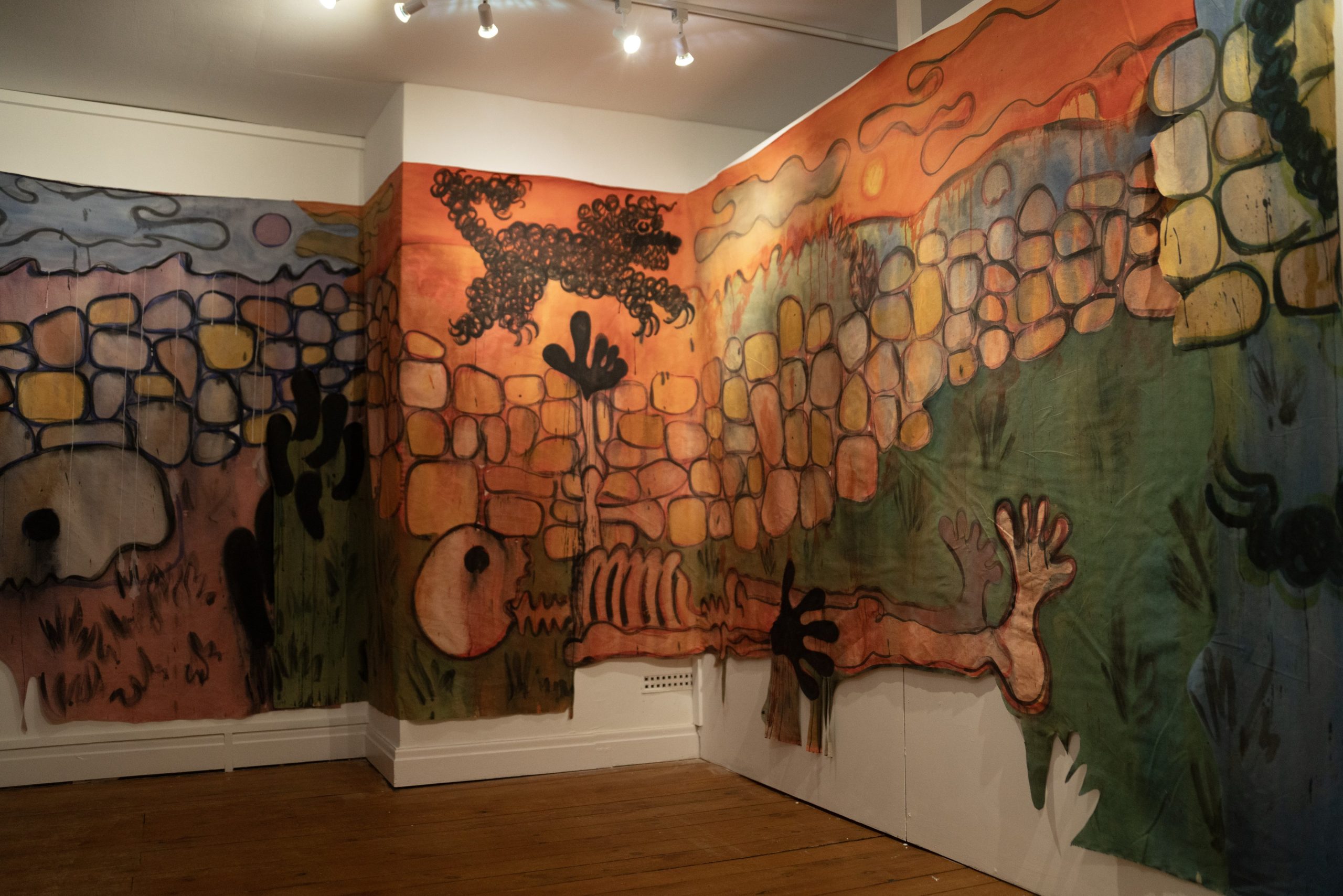 A large painting stretched over a number of walls, curved around bends, of a skeletal figure lying beneath a drystone wall whilst a scruffy dog running around in the field beyond.