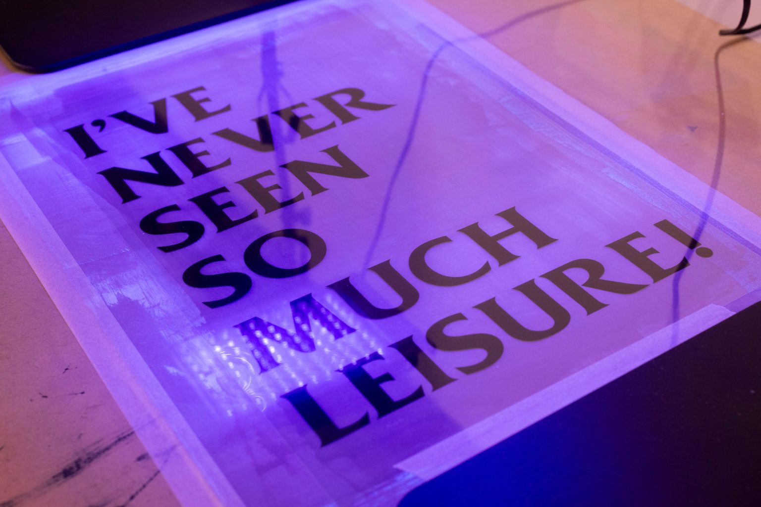 A large typographic print taped to a table, reflecting blue light that shines on it from above.