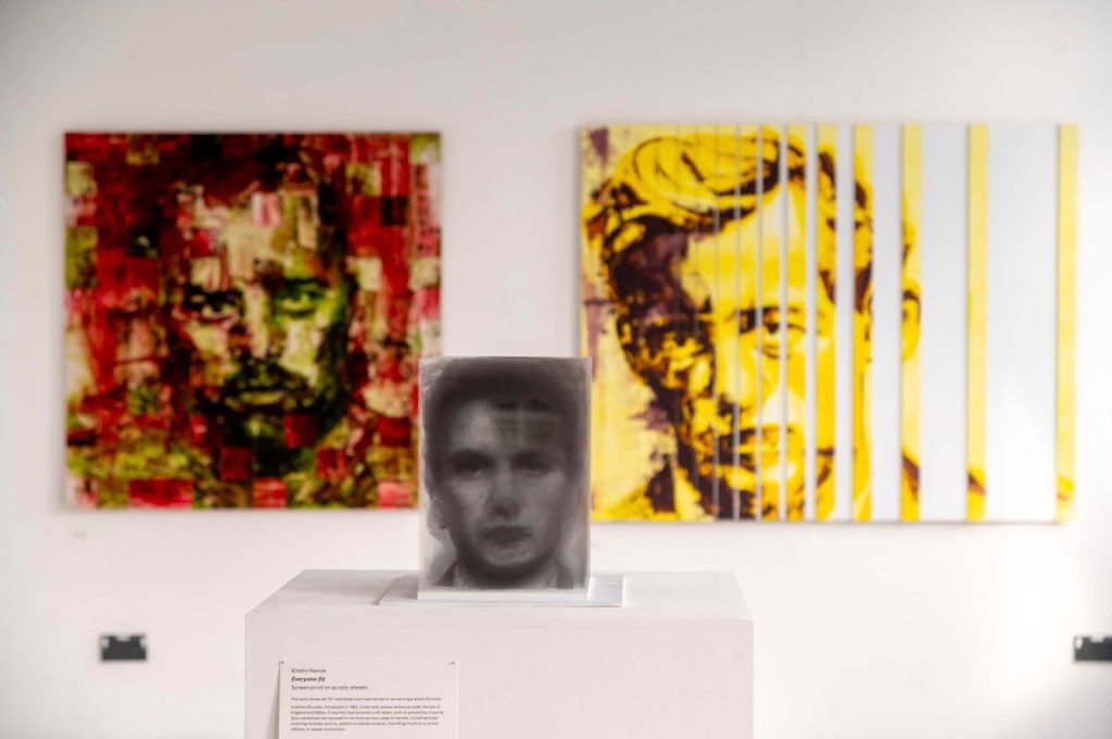 White gallery wall. Three painted portraits displayed. close together. In shades of monochrome and slightly contrasting shades. Serious male faces.