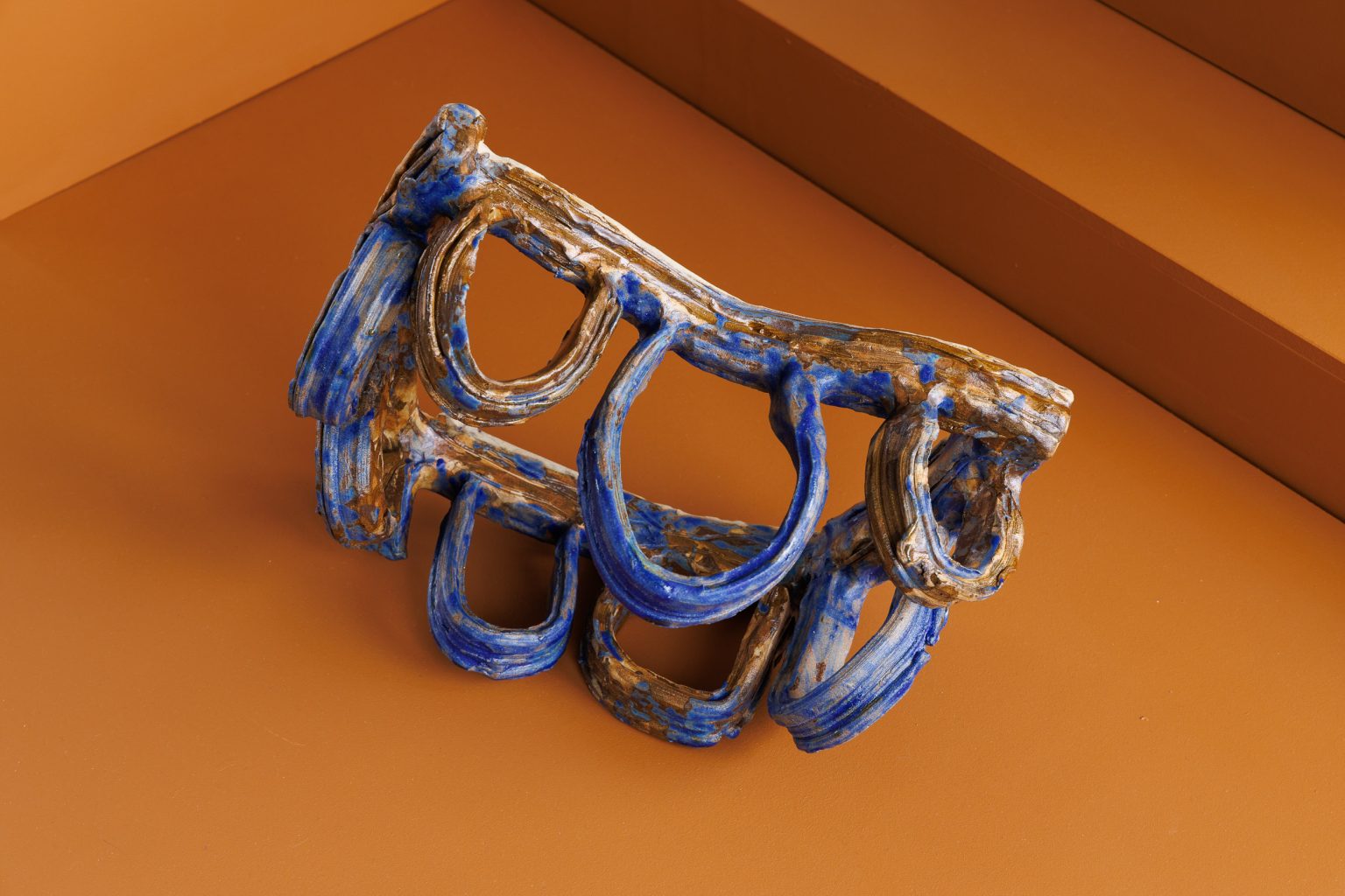 blue ceramic sculpture of loops like a knuckle duster on a sienna background