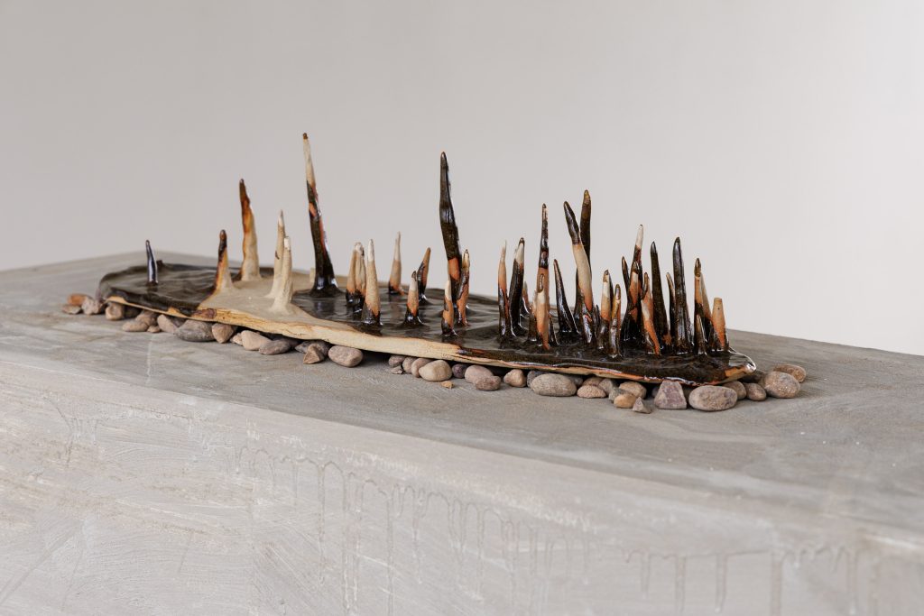a ceramic sculpture of upright spikes on a bed of pebbles on a grey surface