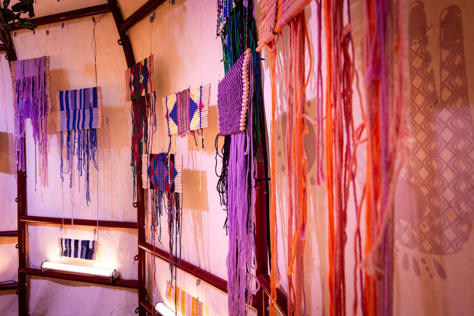 small woven textiles in purples, blues, oranges and pinks hand inside the tent structure