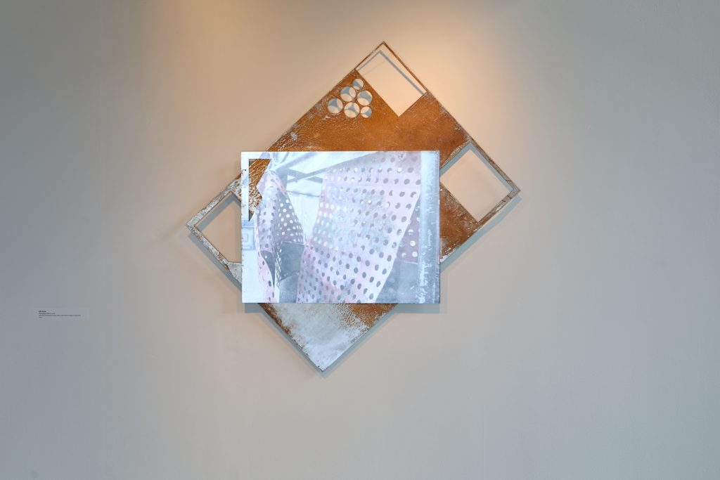 Layered metal sheets collaged into a wall assemblage, with holes and other shapes cut out all referneceing an image printed on the top layer of industrial materials
