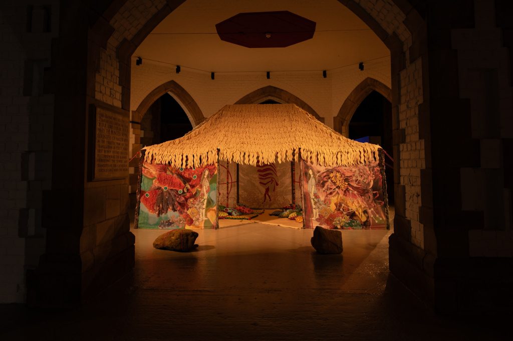 A low tent with multicoloured fabric panels erected in the dimly lit crypt