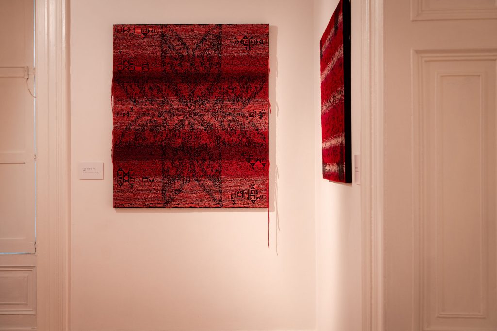 Two red woven tapestries with faint white lines and black patterns in the shape of a star hung on white walls