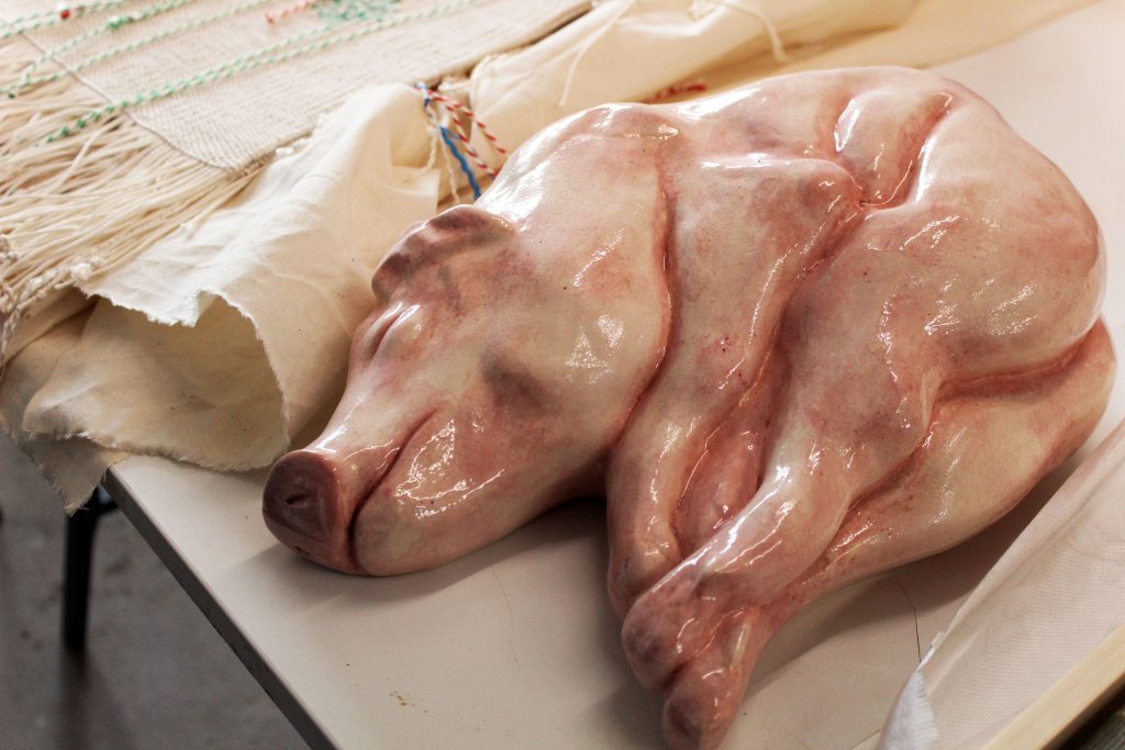 A large pink ceramic pig curled up on a work bench.