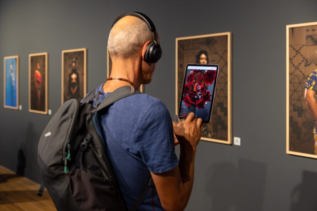 A viewer looks at augmented reality of a portrait on a tablet which shows blooming red flowers