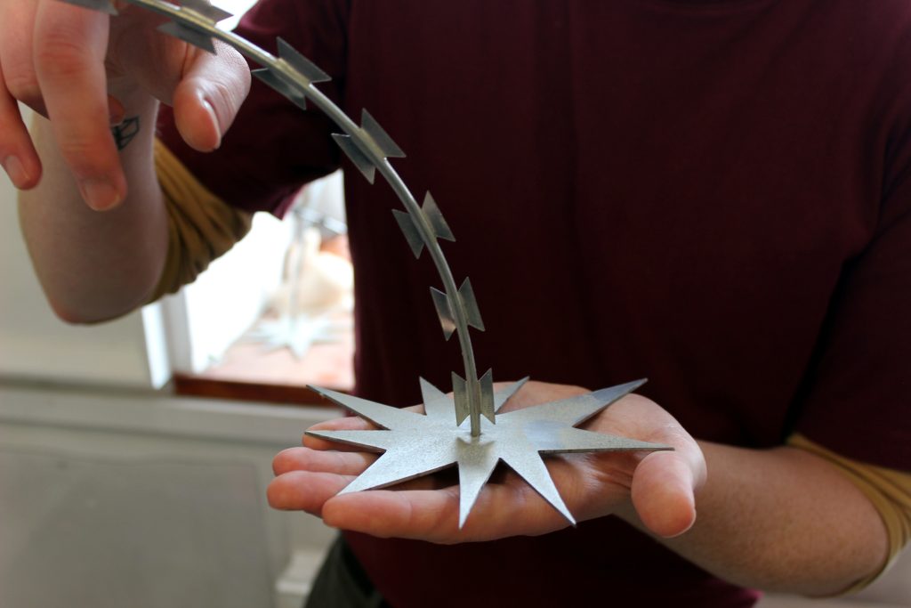 An artist holds a spiky metal sculpture with a stem made from razor wire.