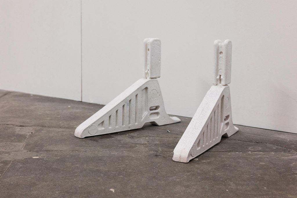 Two cast objects in a white wall galler space. They are stands for road signs, but as a pair look like heeled shoes.